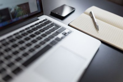 Aufgeschlagenes Notizbuch mit handschriftlichen Notizen neben Laptop auf Holztisch